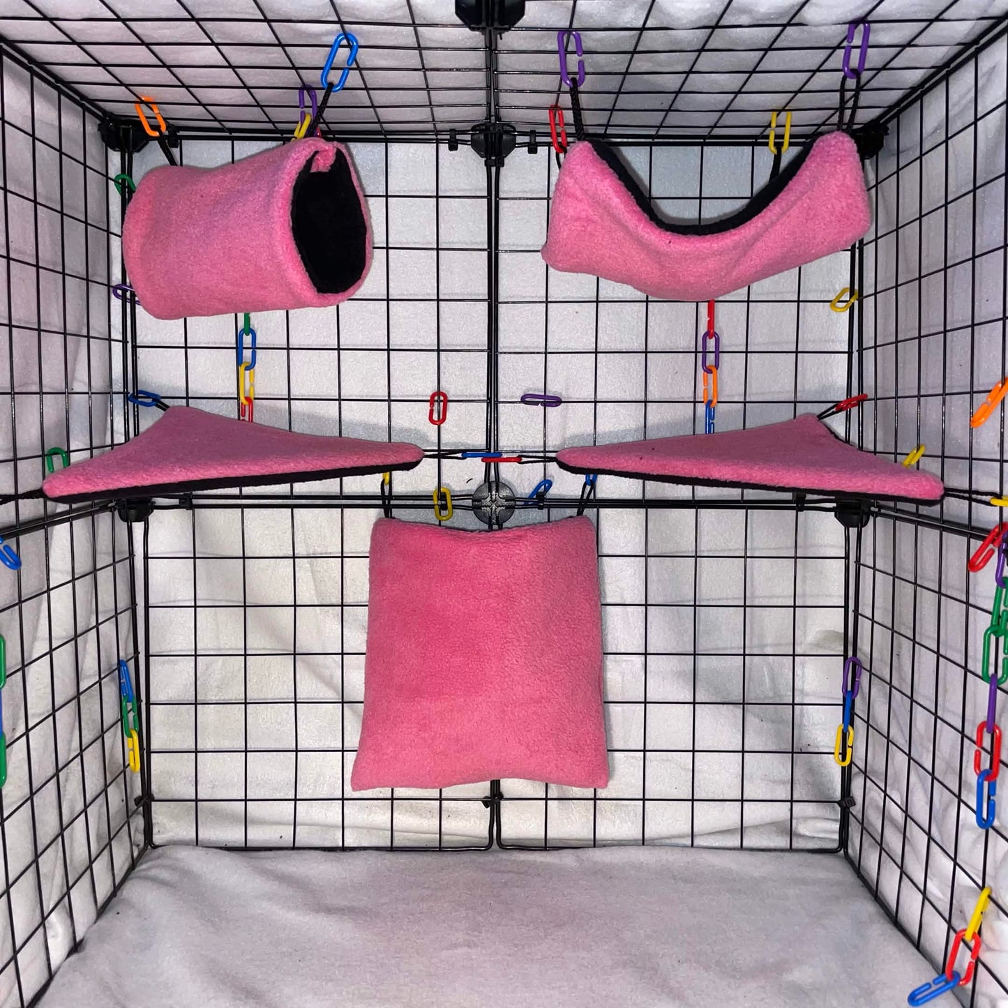 Pink sugar glider cage set with black interior, hammocks, tunnel, pouch, and corner shelves shown in a display cage.