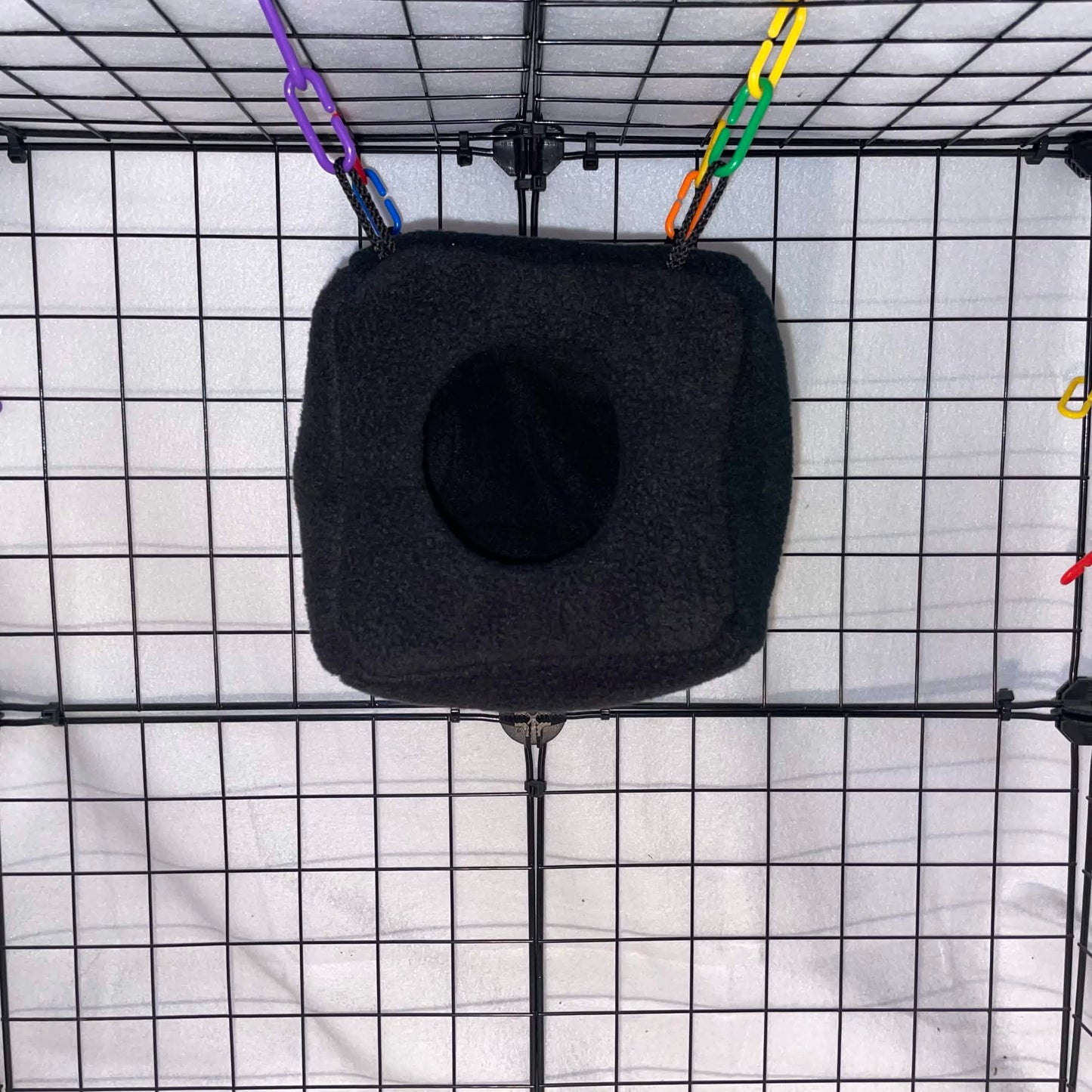 Black fleece sugar glider cube with black interior hanging inside a display cage.