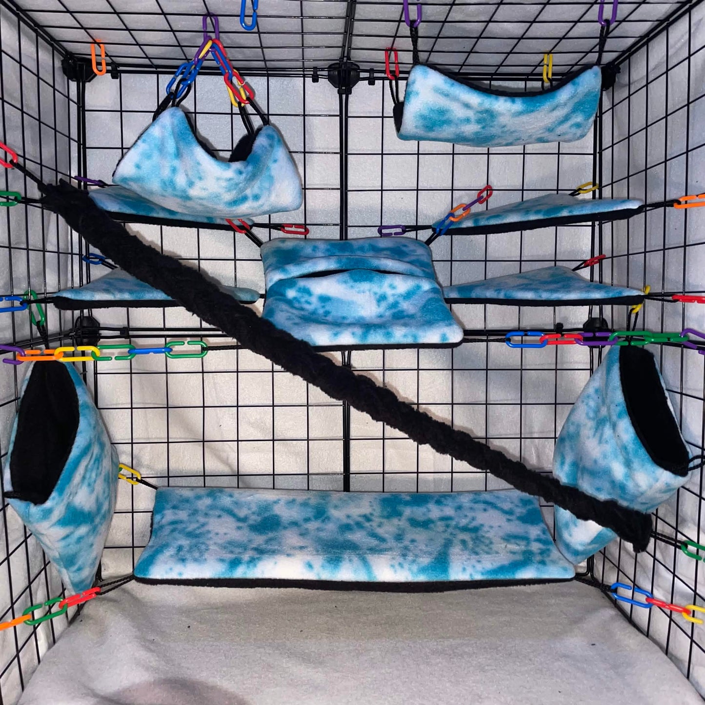 Blue sky tie-dye sugar glider cage set with fleece hammocks, pouches, shelves, and black braided rope installed in a wire cage.
