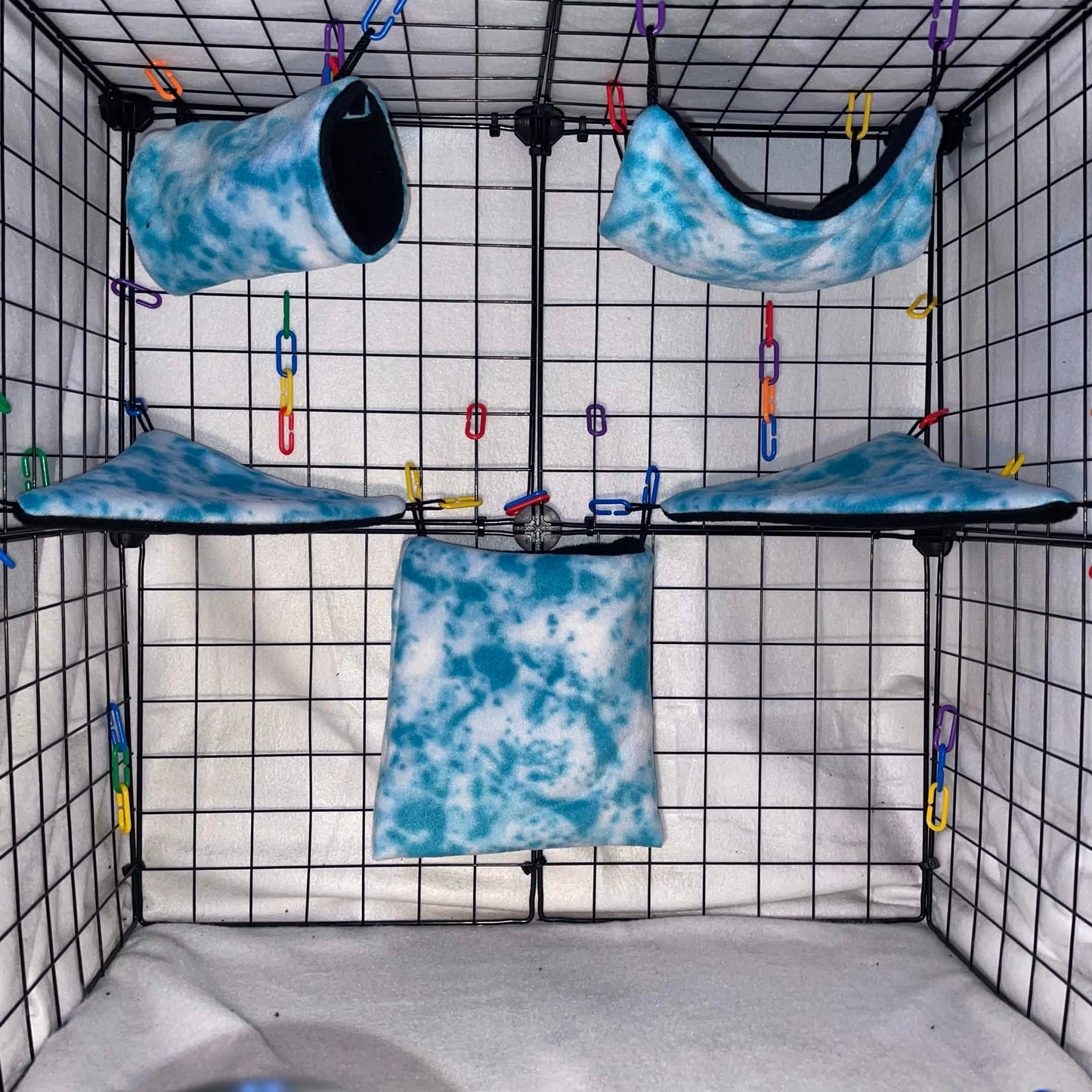 Blue sky tie-dye sugar glider expansion cage set with fleece hammocks, pouches, shelves, and black braided rope, installed in display cage. 