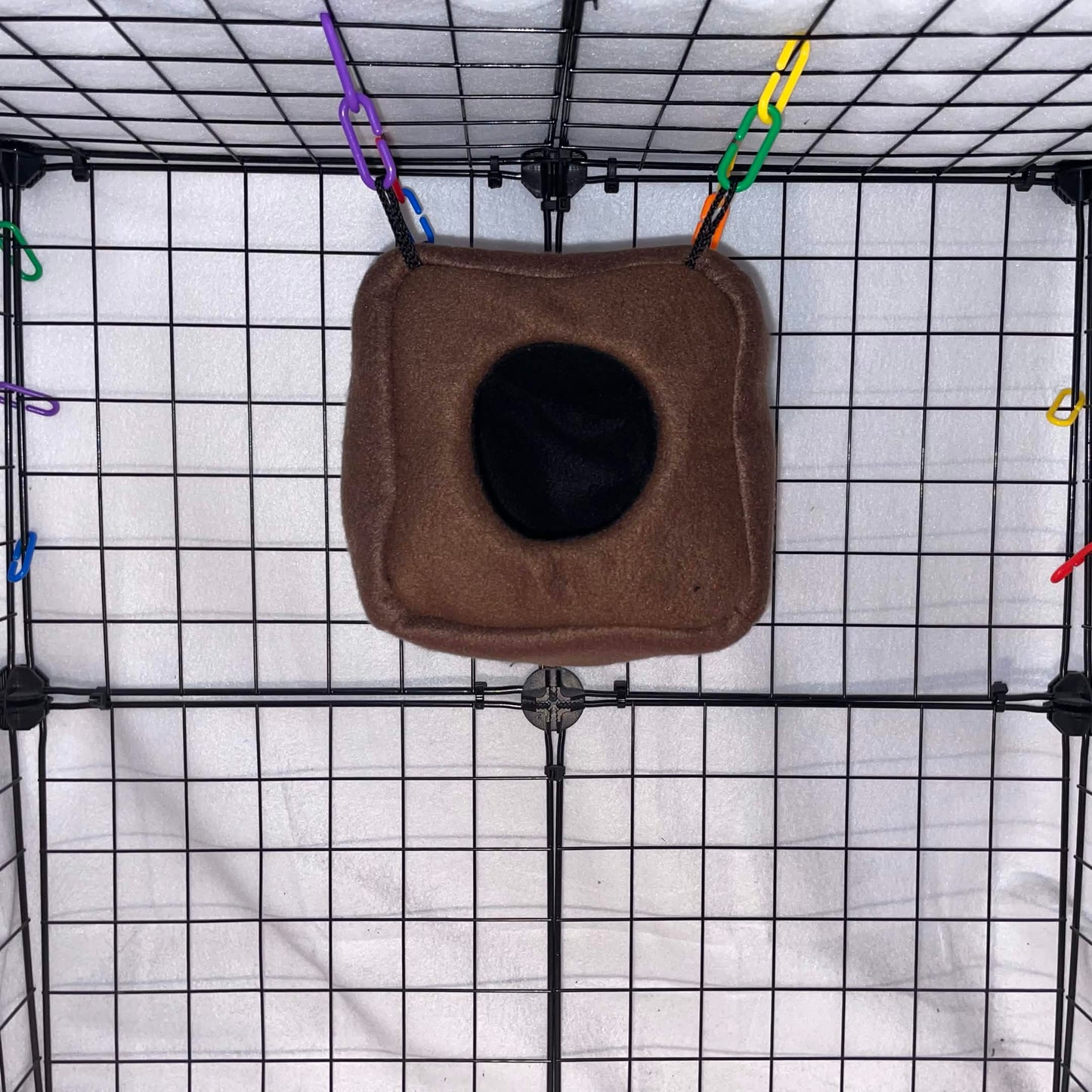 Brown sugar glider fleece cube hideout with black opening hanging in a wire cage.