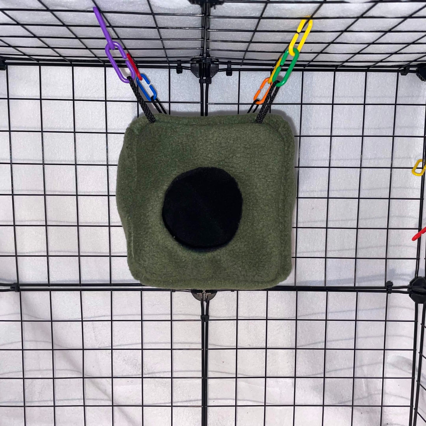 Forest green sugar glider fleece cube hideout with black opening hanging in a wire cage.