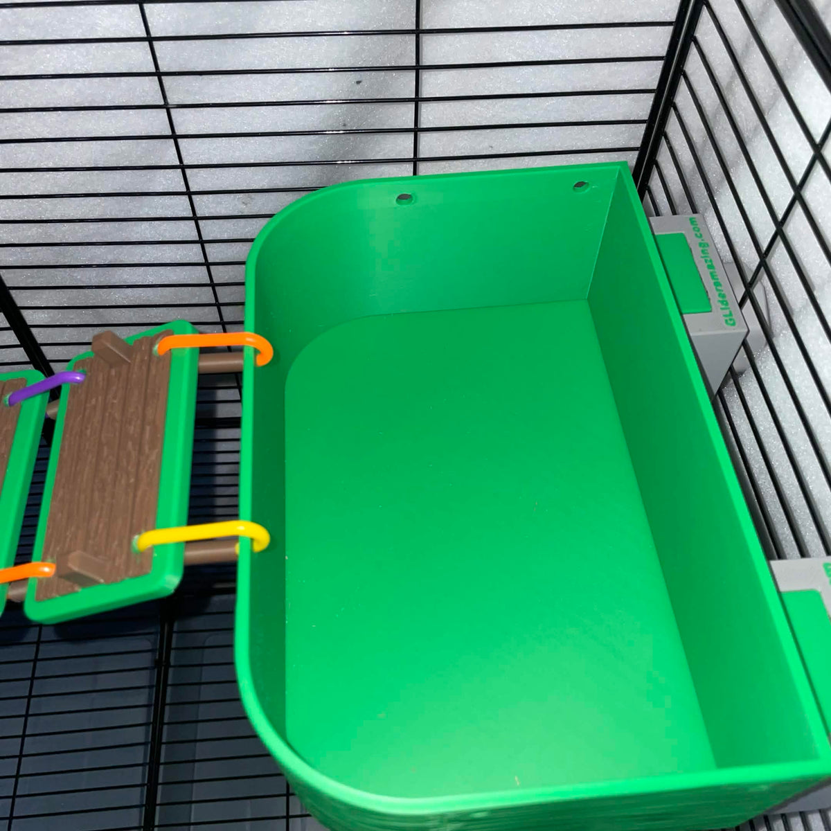 Top view of an empty green sugar glider ball pit basket with a boardwalk bridge attached.