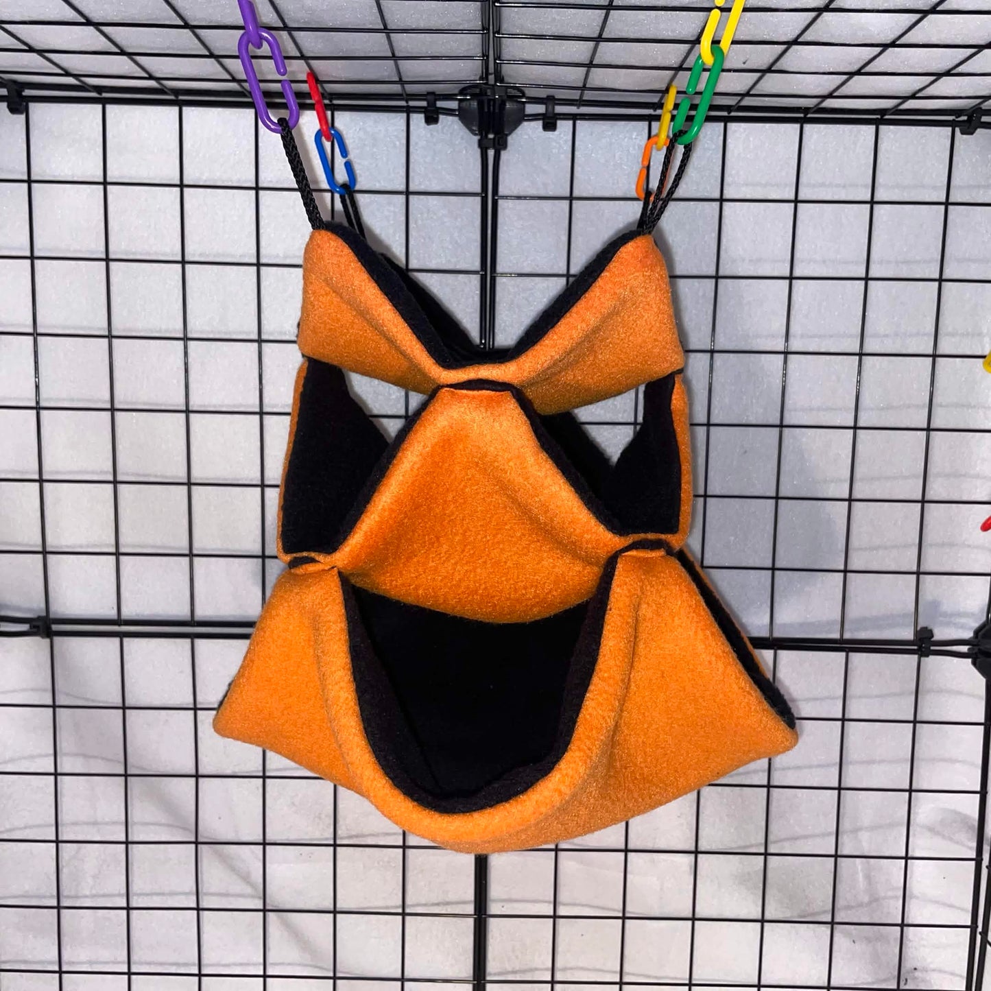 Orange sugar glider 3-tier honeycomb hammock with black interior hanging in a wire cage.