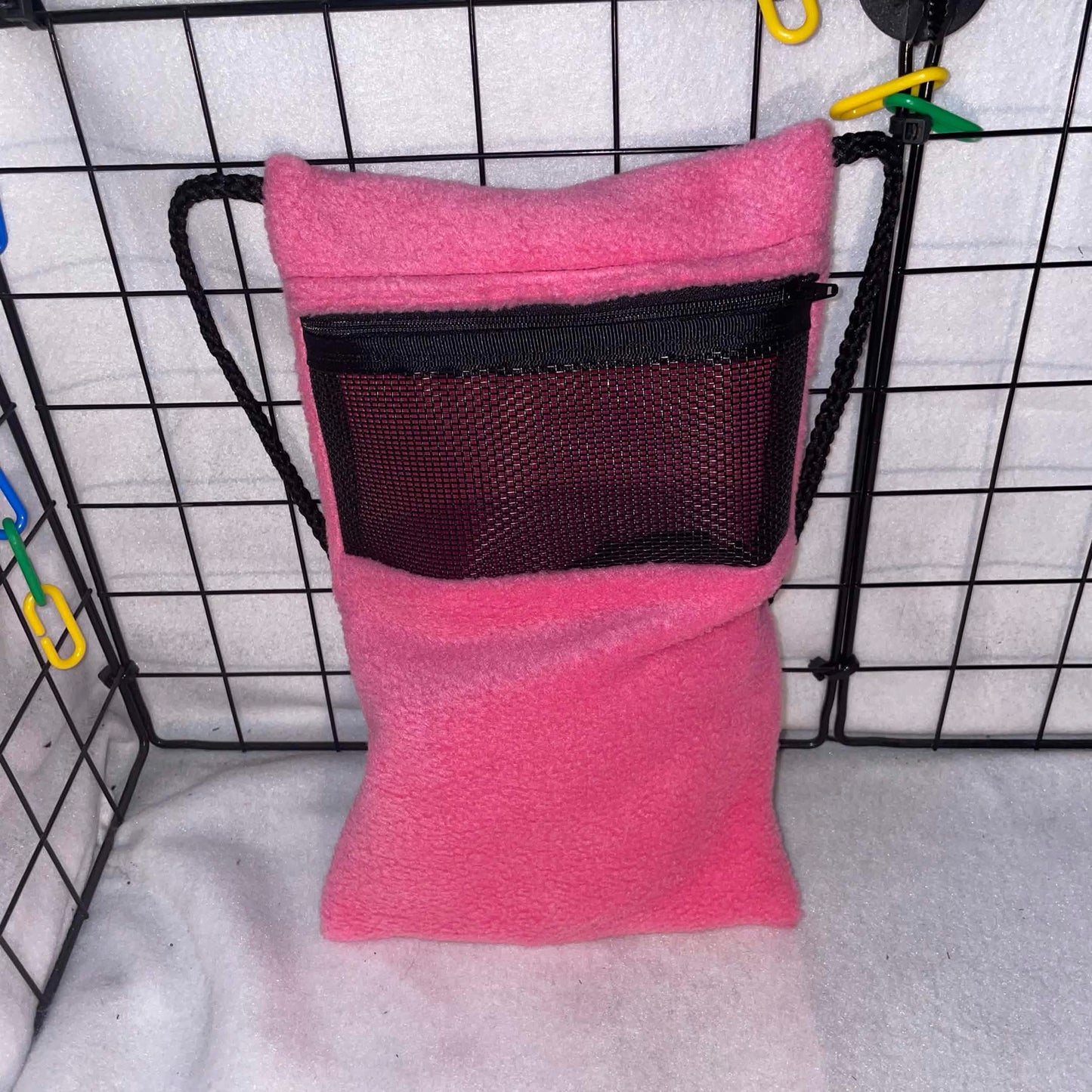 Pink fleece sugar glider bonding pouch with black mesh window and shoulder strap shown inside a display cage.