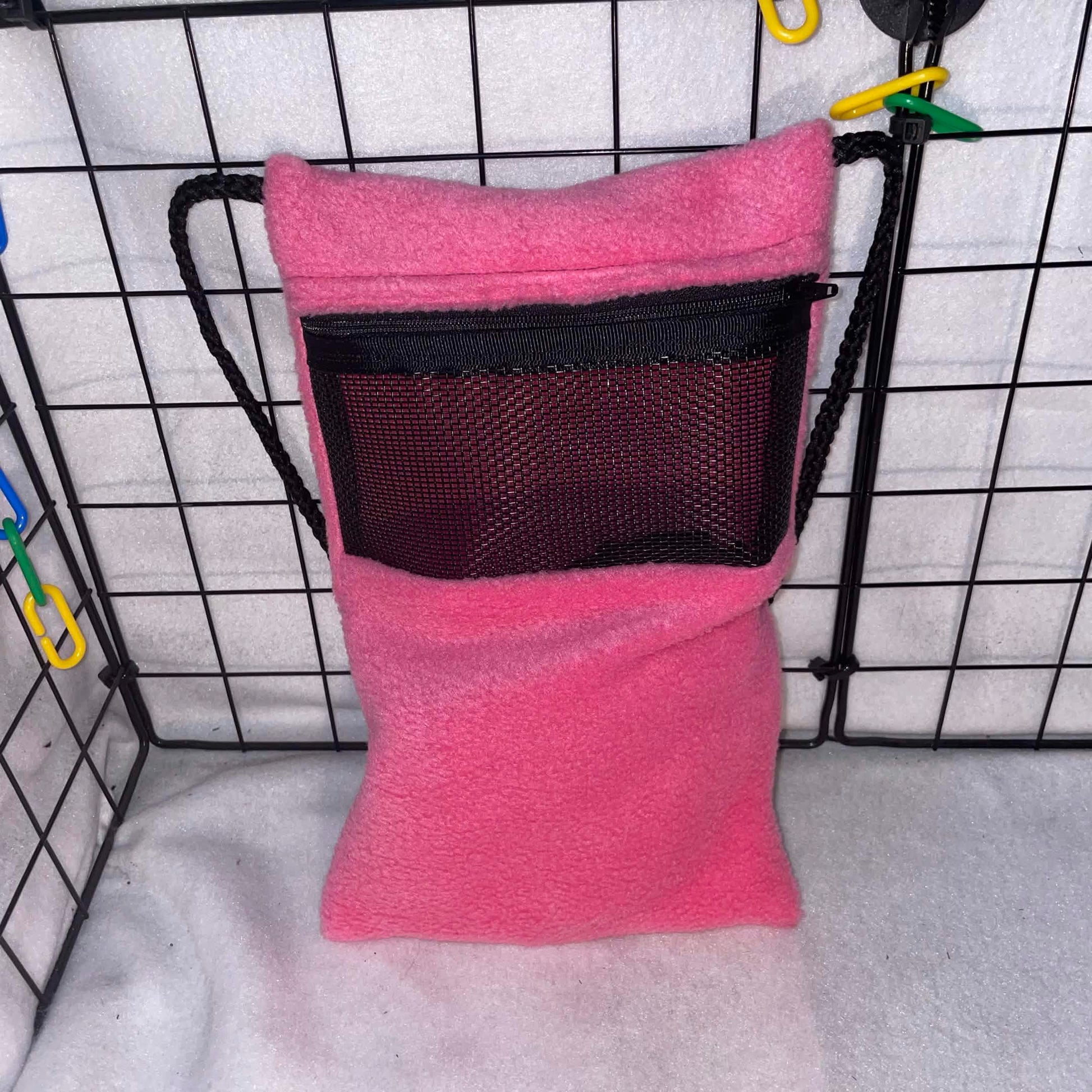 Pink fleece sugar glider bonding pouch with black mesh window and shoulder strap shown inside a display cage.