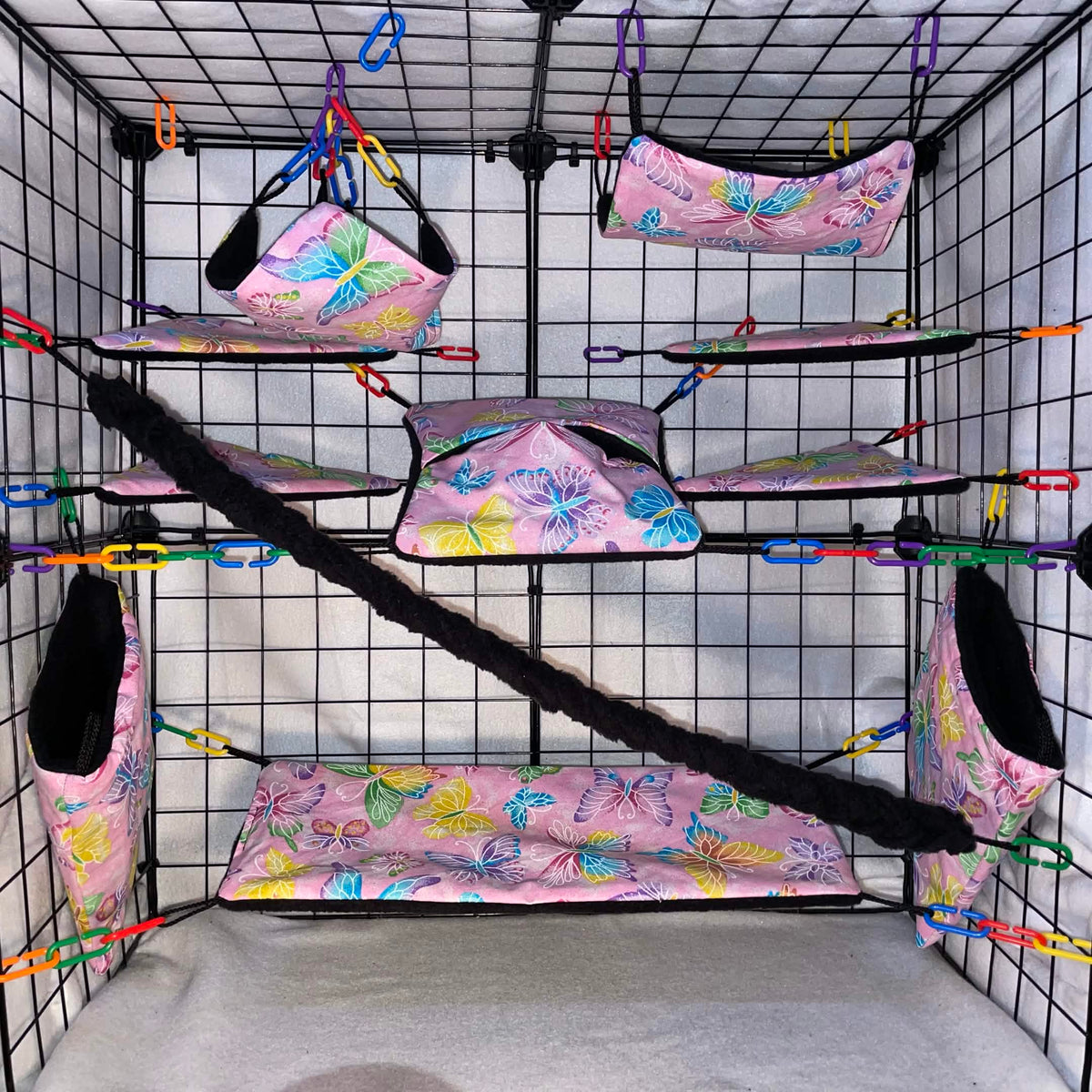 Pink butterfly print sugar glider cage set in a display cage with hammocks, pouches, bridge, black fleece vine, and black interior.