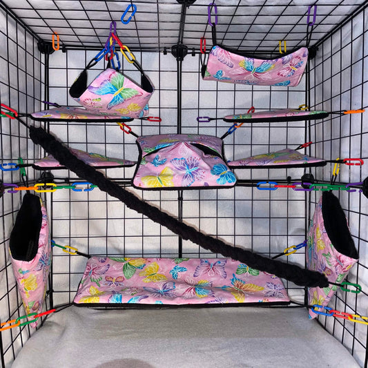 Pink butterfly print sugar glider cage set in a display cage with hammocks, pouches, bridge, black fleece vine, and black interior.