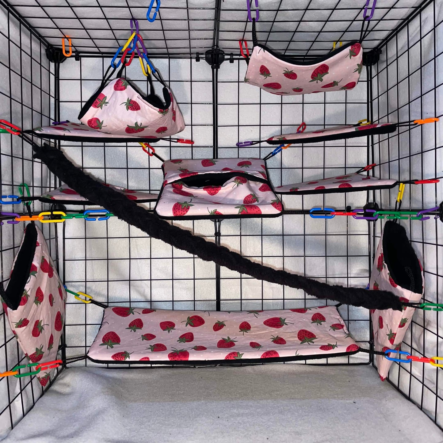Pink strawberry sugar glider cage set with black fleece for interior of pouches, hammocks, shelves, bridge, and braided rope inside a display cage.