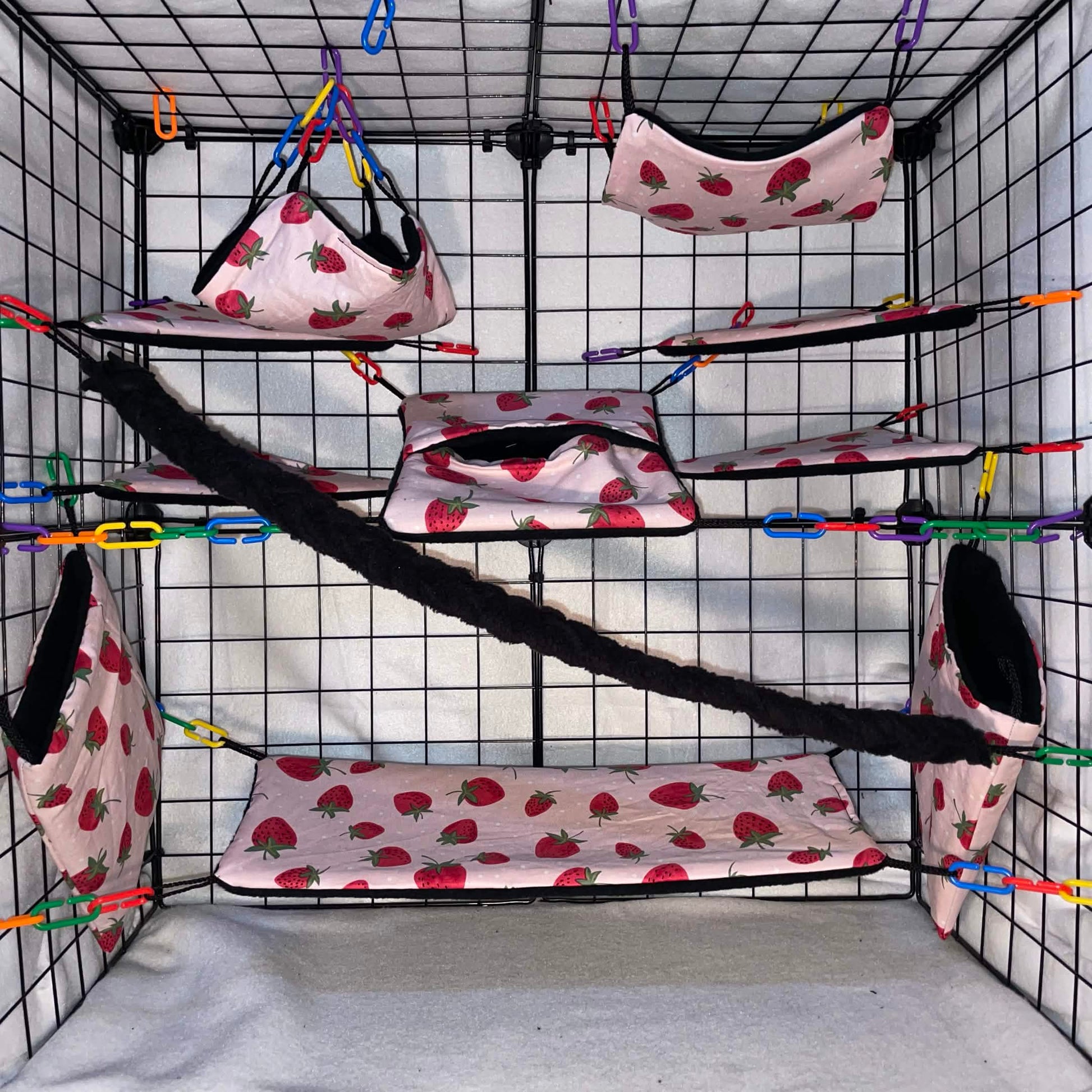 Pink strawberry sugar glider cage set with black fleece for interior of pouches, hammocks, shelves, bridge, and braided rope inside a display cage.