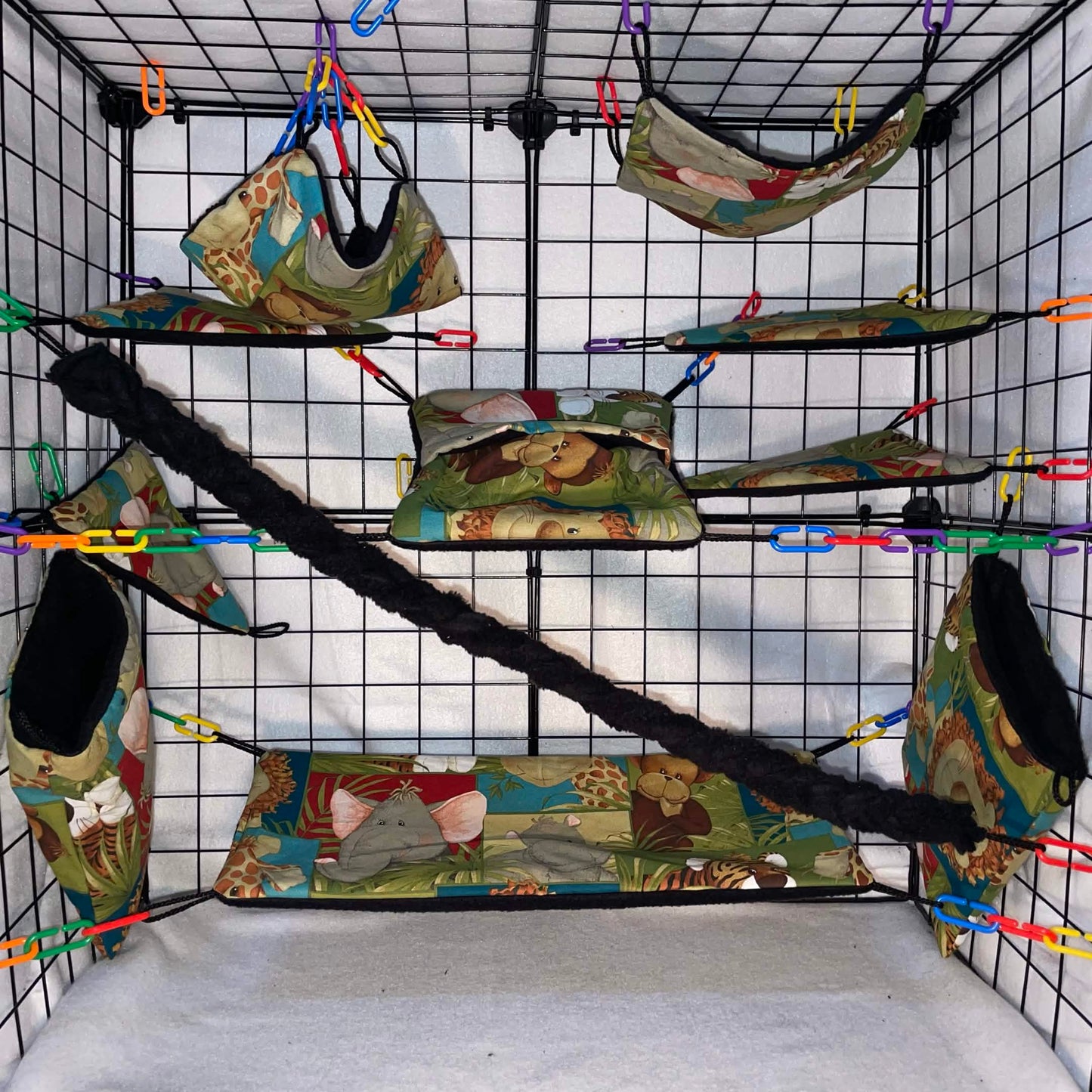 Safari animal print sugar glider cage set with black interior of pouches, hammocks, shelves, bridge, and braided rope inside a display cage.