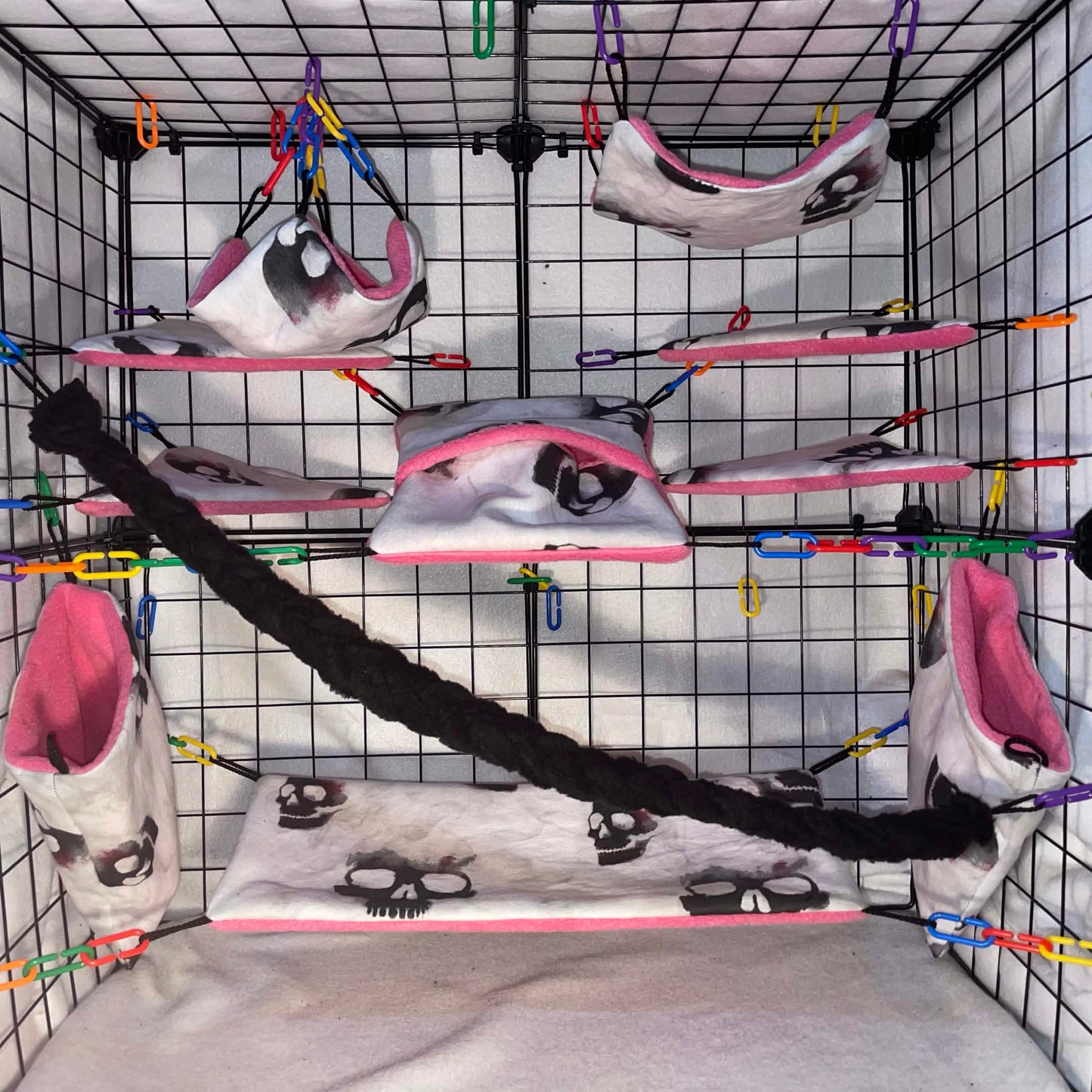Skull print sugar glider cage set with pink interior, hammocks, tunnels, shelves, pouch, and black braided rope shown in a display cage.