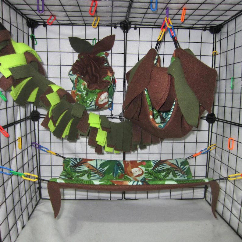 Sloth jungle print sugar glider cage set with brown and green fleece hammock, pouch, shelf, fleece vine, and leaf accents installed in a wire cage.