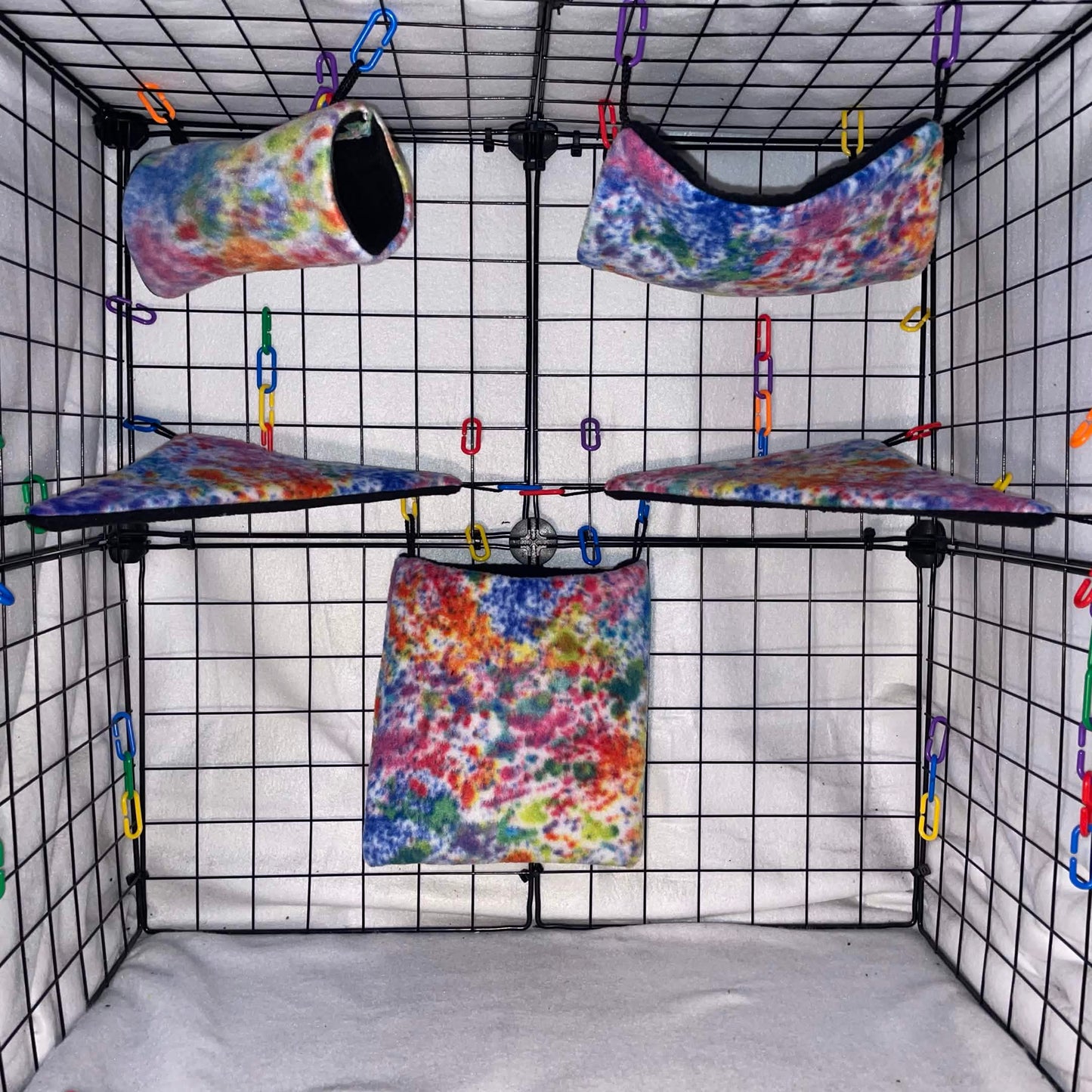 Splatter Paint Rainbow tie-dye sugar glider fleece expansion set with pouch, hammock, tunnel, and corner shelves installed in a wire display cage.