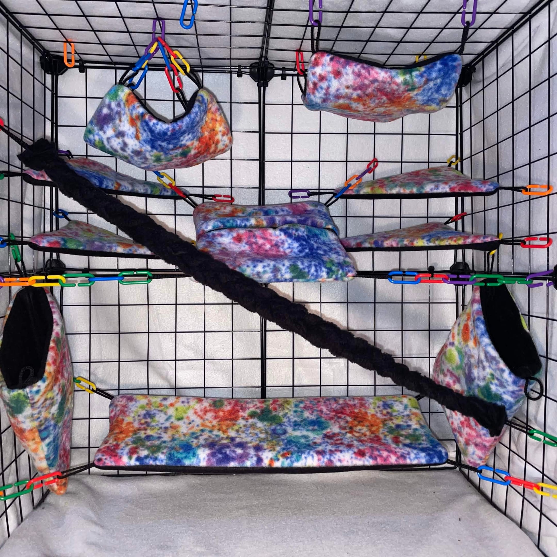 Splatter paint Rainbow tie-dye sugar glider cage set with fleece hammocks, pouches, shelves, and black braided rope installed in a wire display cage.