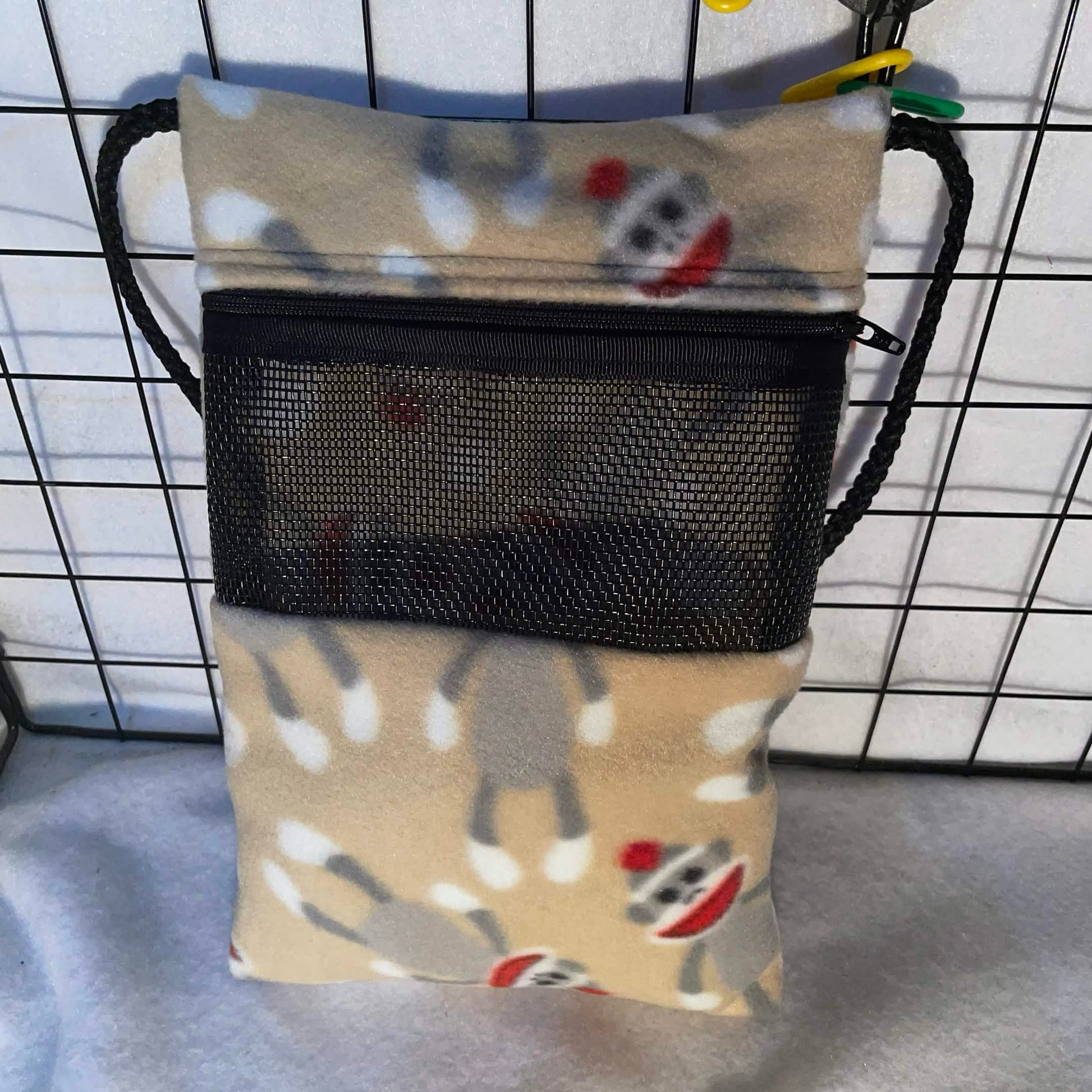 Tan sock monkey print sugar glider bonding pouch with black mesh window and shoulder strap shown inside a display cage.