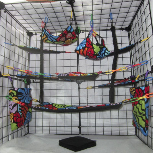 17-piece sugar glider cage set featuring dark floral print fleece and fabric, including square hammocks, Hide N Seek Hammock™, Bouncer Bridge™, cage pouches, Corner Leap Shelves™, fleece blankets, and braided fleece dangling ropes arranged inside a metal cage for small pet comfort and enrichment.