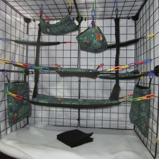 17-piece sugar glider cage set in pine forest print, featuring fleece hammocks, pouches, and accessories arranged inside a metal cage for small pet comfort and enrichment.
